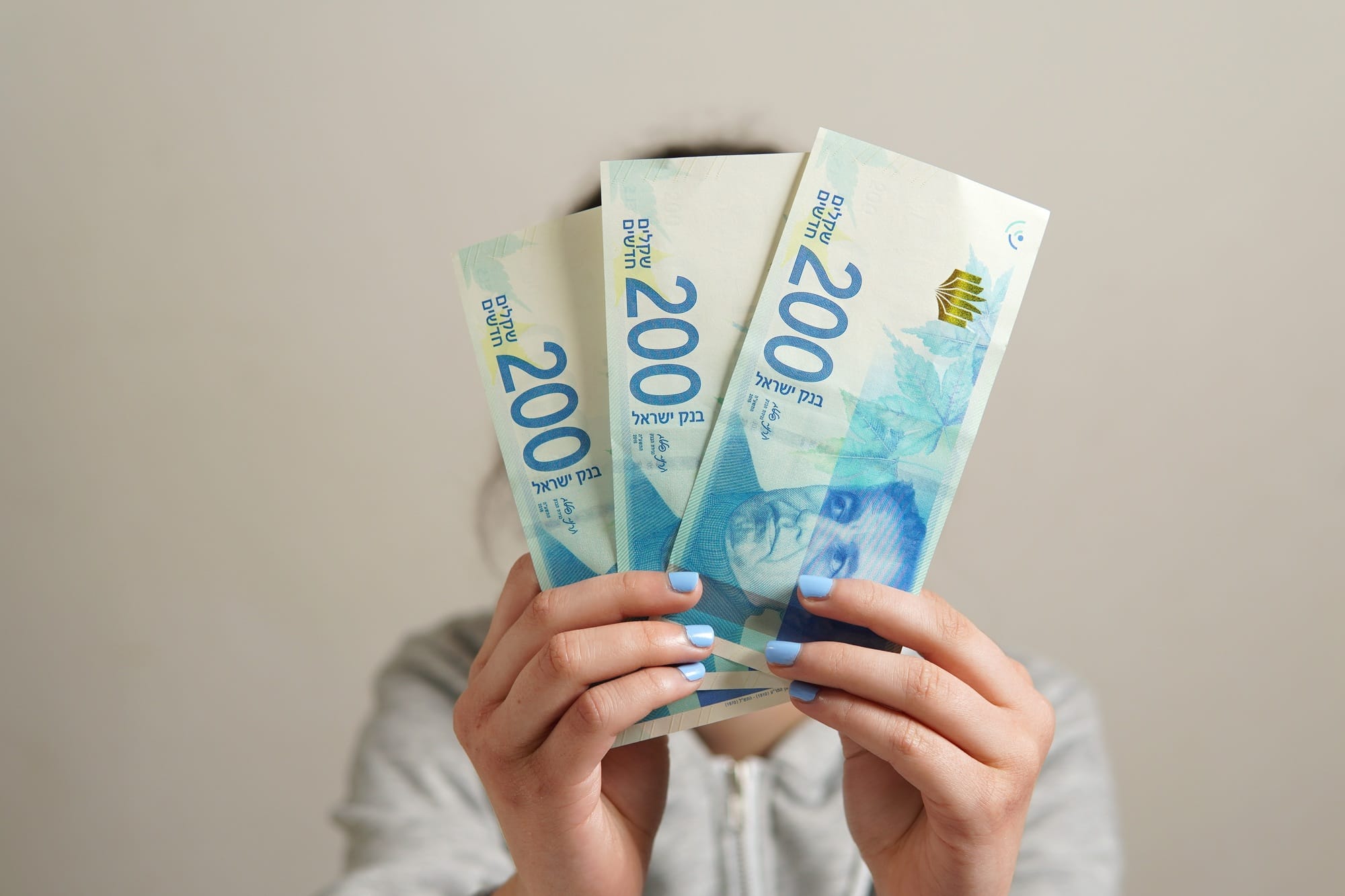 Unrecognizable person holding three 200 Israeli Shekels banknotes - business, finance concept